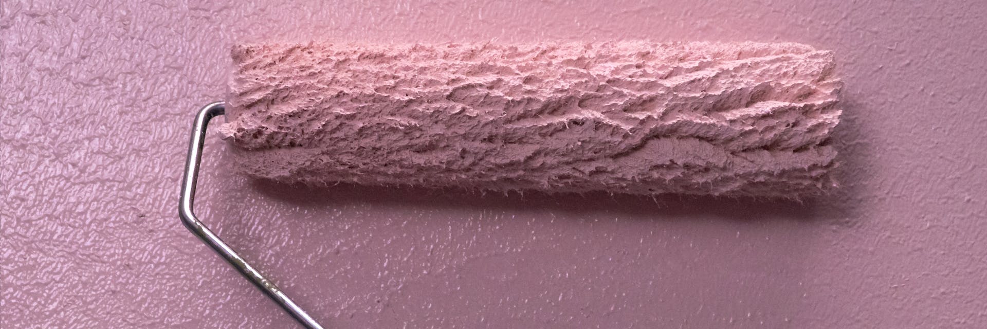 Roller with pink paint on a wall 